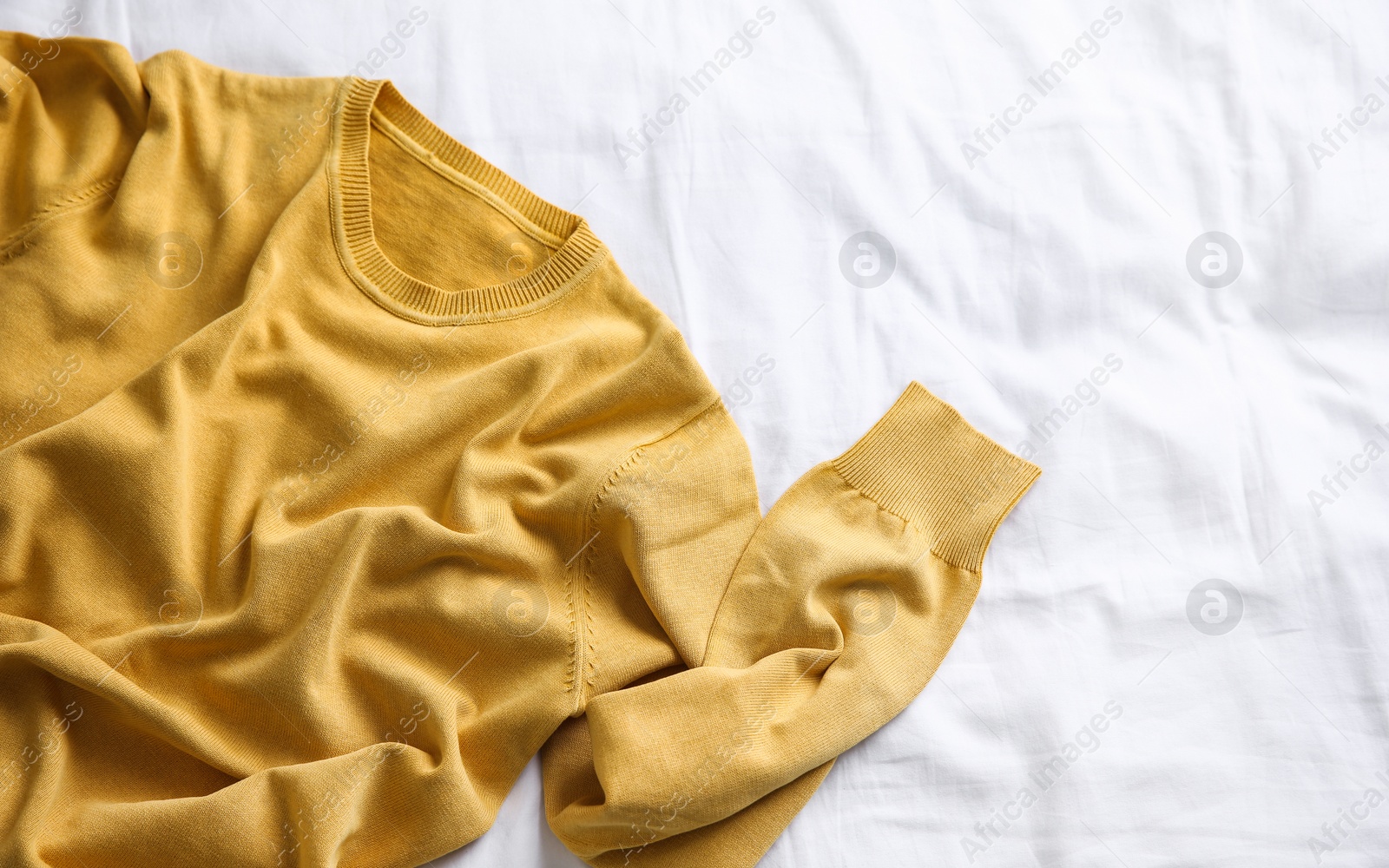 Photo of Yellow warm sweater on white crumpled fabric, top view