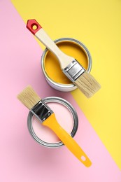 Cans of different paints with brushes on color background, flat lay