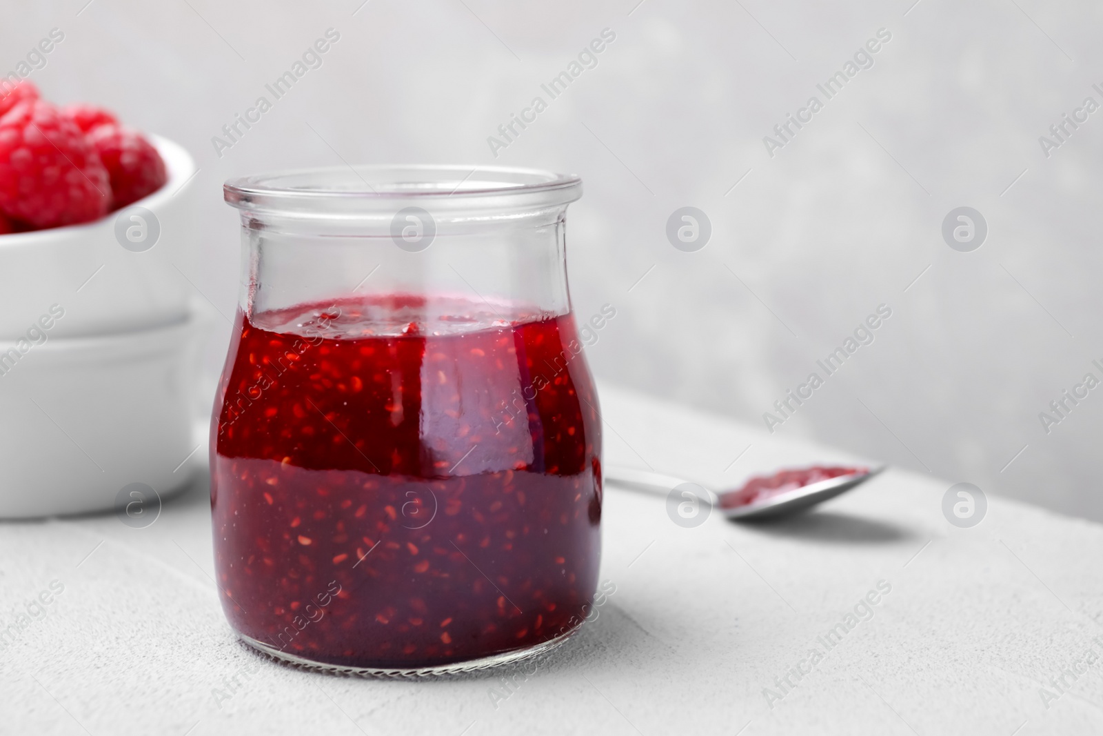 Photo of Delicious jam and fresh raspberries on light table. Space for text