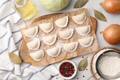 Photo of Raw dumplings (varenyky) with tasty filling and ingredients on light grey table, flat lay