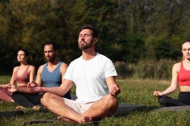 Group of people practicing yoga on mats outdoors. Lotus pose