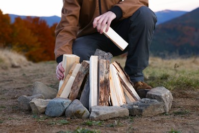 Photo of Traveler making bonfire with dry wood outdoors, closeup