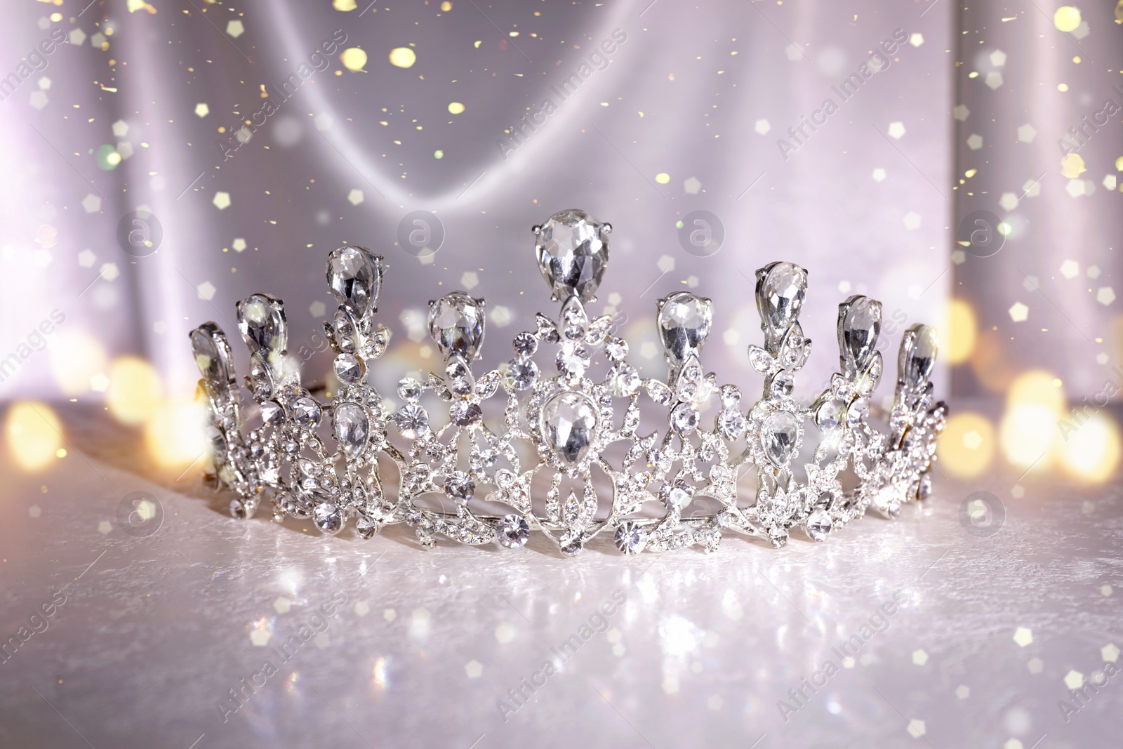 Image of Beautiful silver tiara with diamonds on white table, bokeh effect