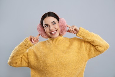 Photo of Beautiful young woman wearing earmuffs on light grey background