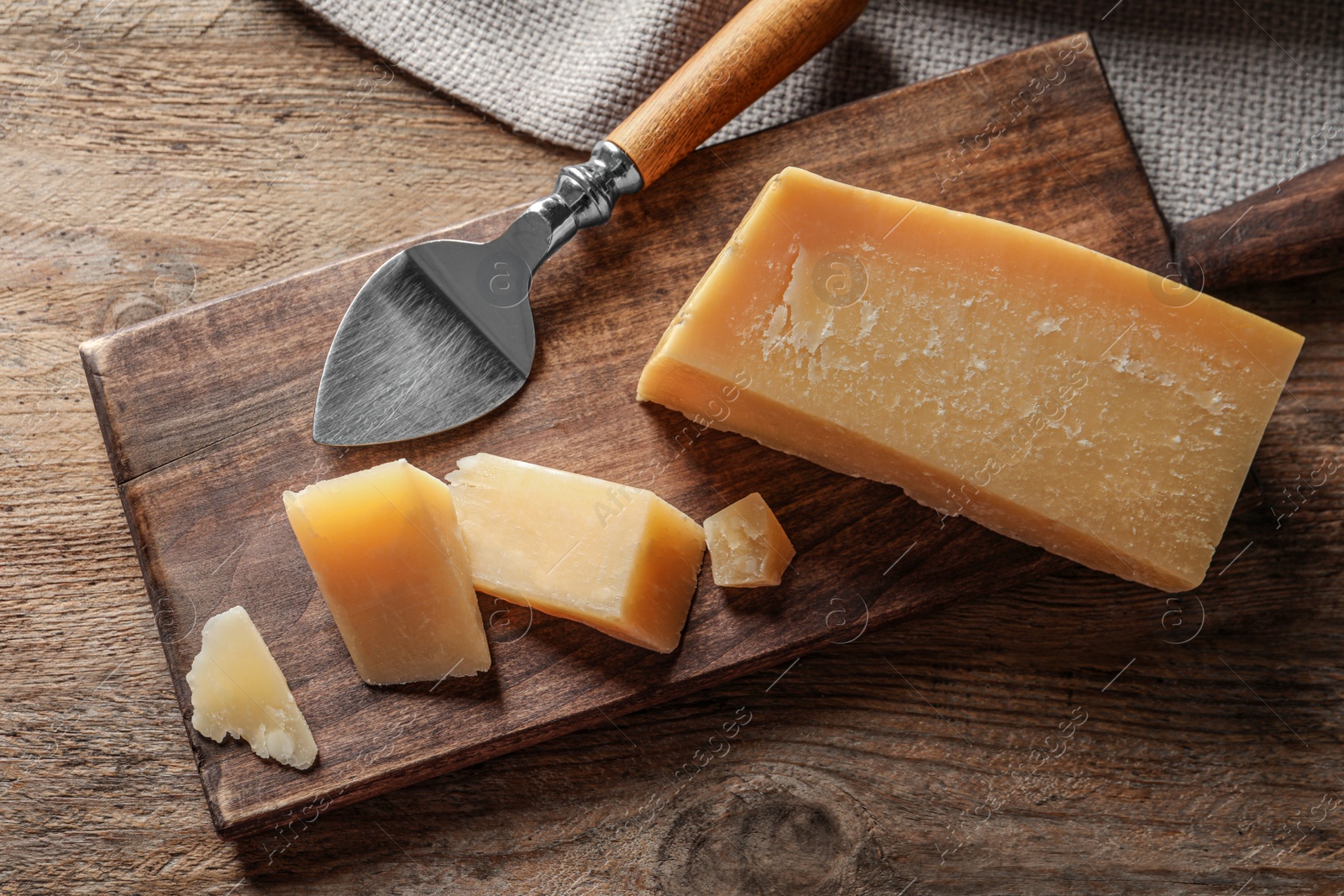 Photo of Board with cut Parmesan cheese on wooden table, top view