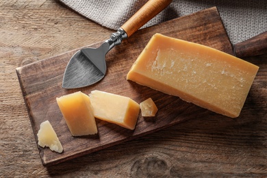 Photo of Board with cut Parmesan cheese on wooden table, top view