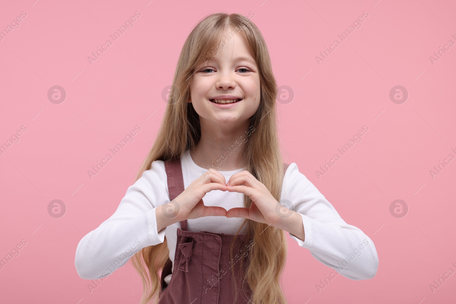 Photo of Happy girl showing heart gesture with hands on pink background