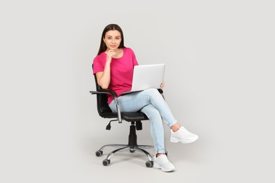 Photo of Young woman with laptop sitting in comfortable office chair on grey background