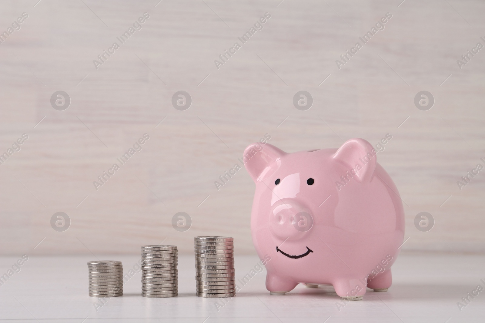 Photo of Financial savings. Piggy bank and stacked coins on white wooden table