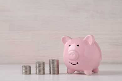 Financial savings. Piggy bank and stacked coins on white wooden table