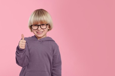Photo of Cute little boy in glasses showing thumbs up on pink background, space for text