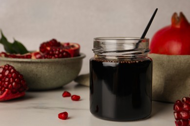 Photo of Glass jar of tasty pomegranate sauce on white marble table. Space for text