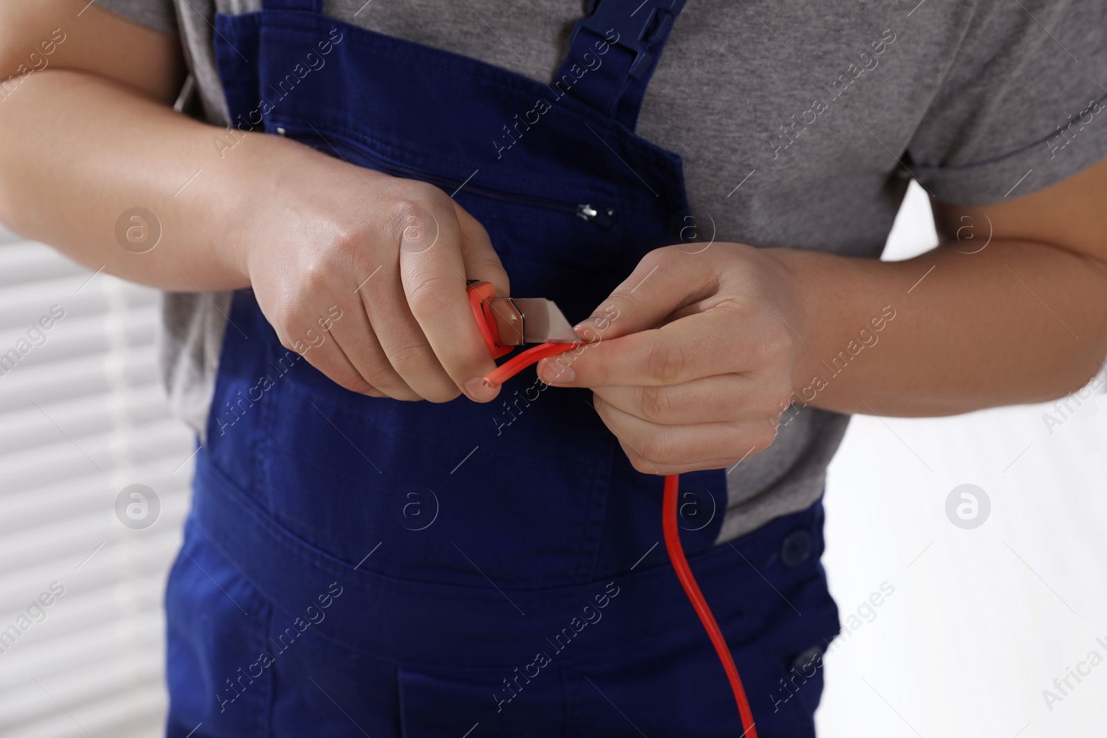 Photo of Professional electrician in uniform stripping wiring indoors, closeup