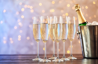 Photo of Glasses with champagne and bottle in bucket on table against blurred lights