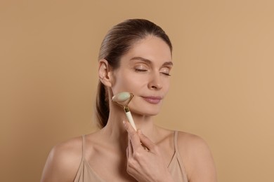 Woman massaging her face with jade roller on beige background