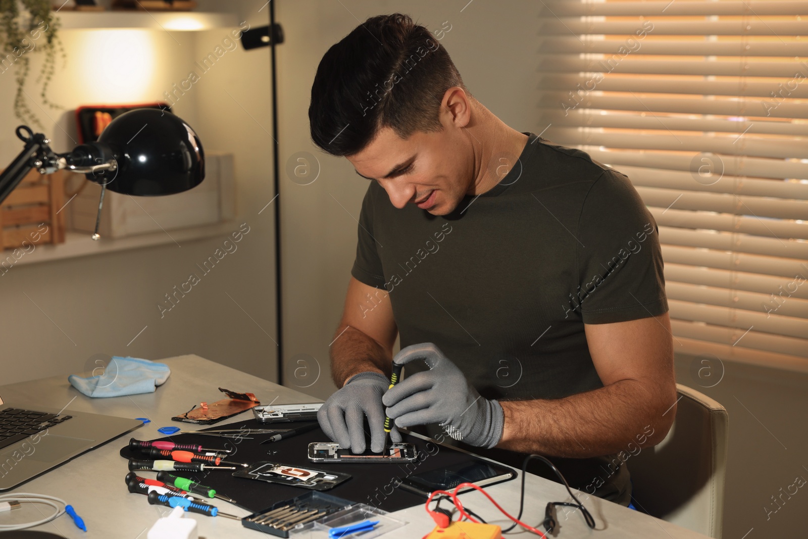 Photo of Technician repairing broken smartphone at table indoors