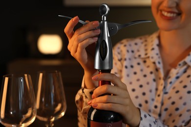 Photo of Romantic dinner. Woman opening wine bottle with corkscrew indoors, closeup