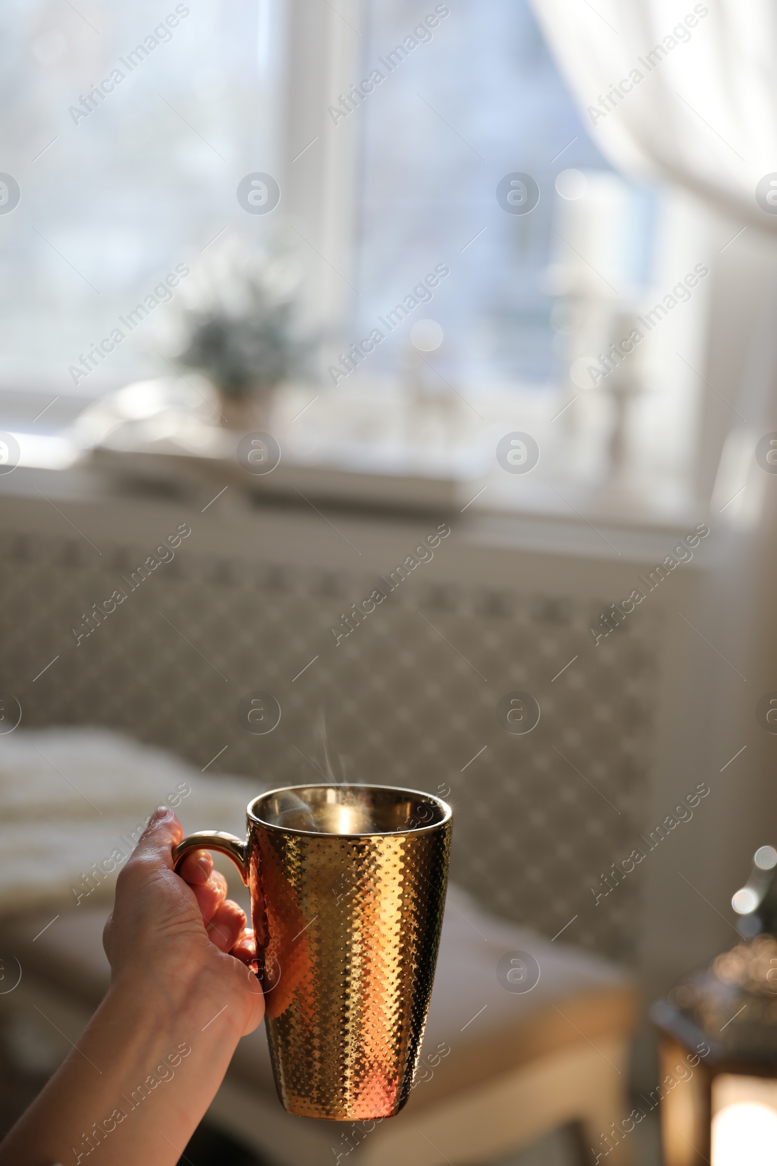 Photo of Woman with golden cup of hot drink in room decorated for Christmas, closeup