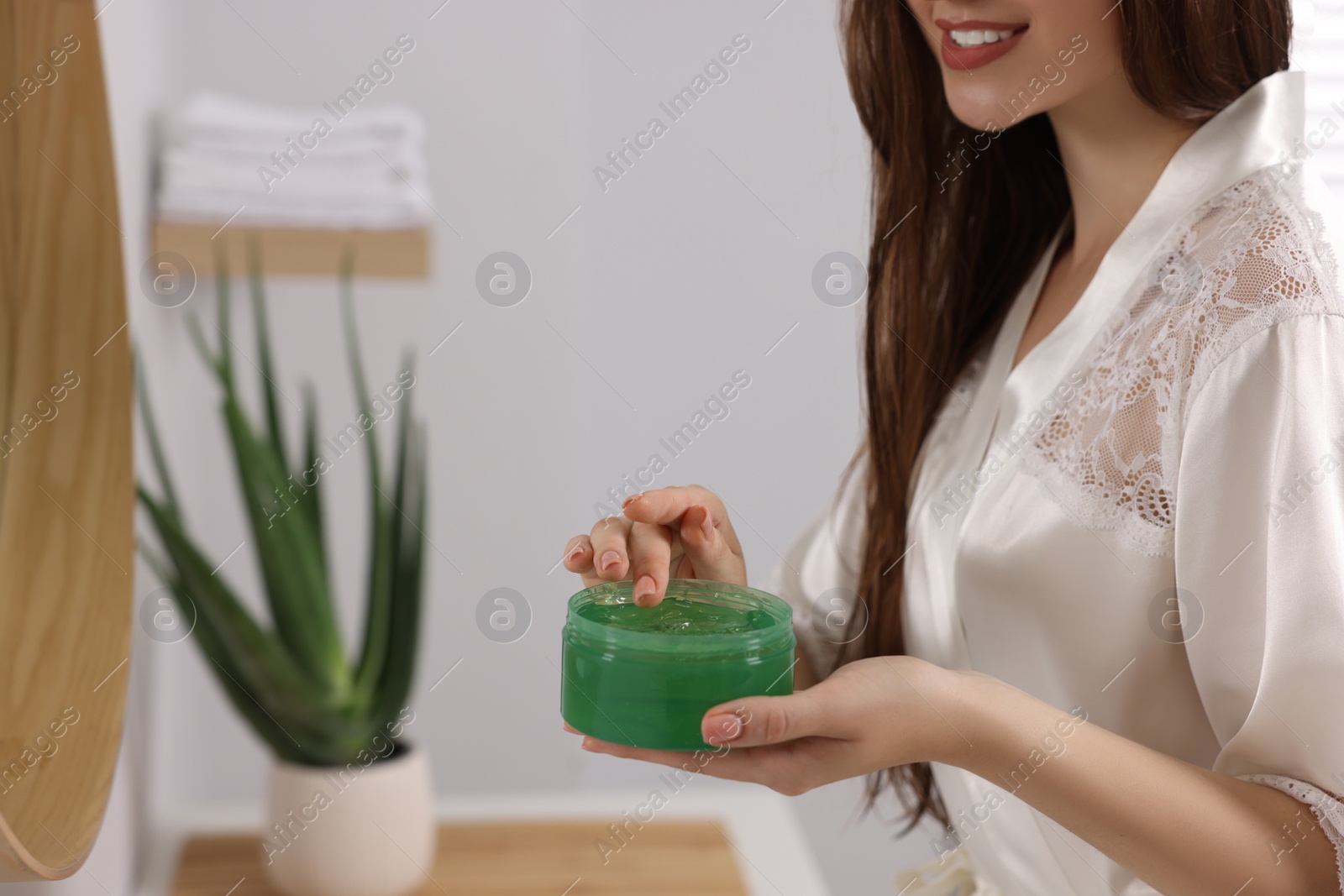 Photo of Young woman holding jar of aloe hair mask indoors, closeup. Space for text