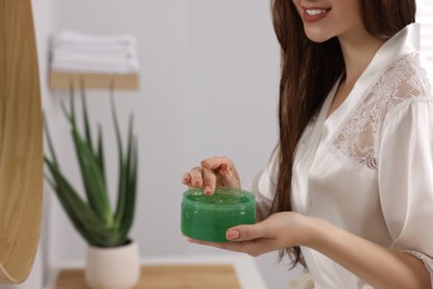 Young woman holding jar of aloe hair mask indoors, closeup. Space for text