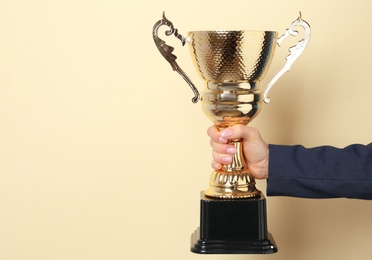 Photo of Woman holding golden trophy cup on color background, closeup. Space for text