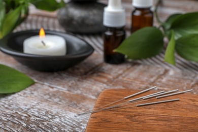 Photo of Wooden board with needles for acupuncture on table, closeup