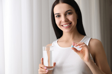 Photo of Young woman with glass of water and vitamin pill on light background. Space for text