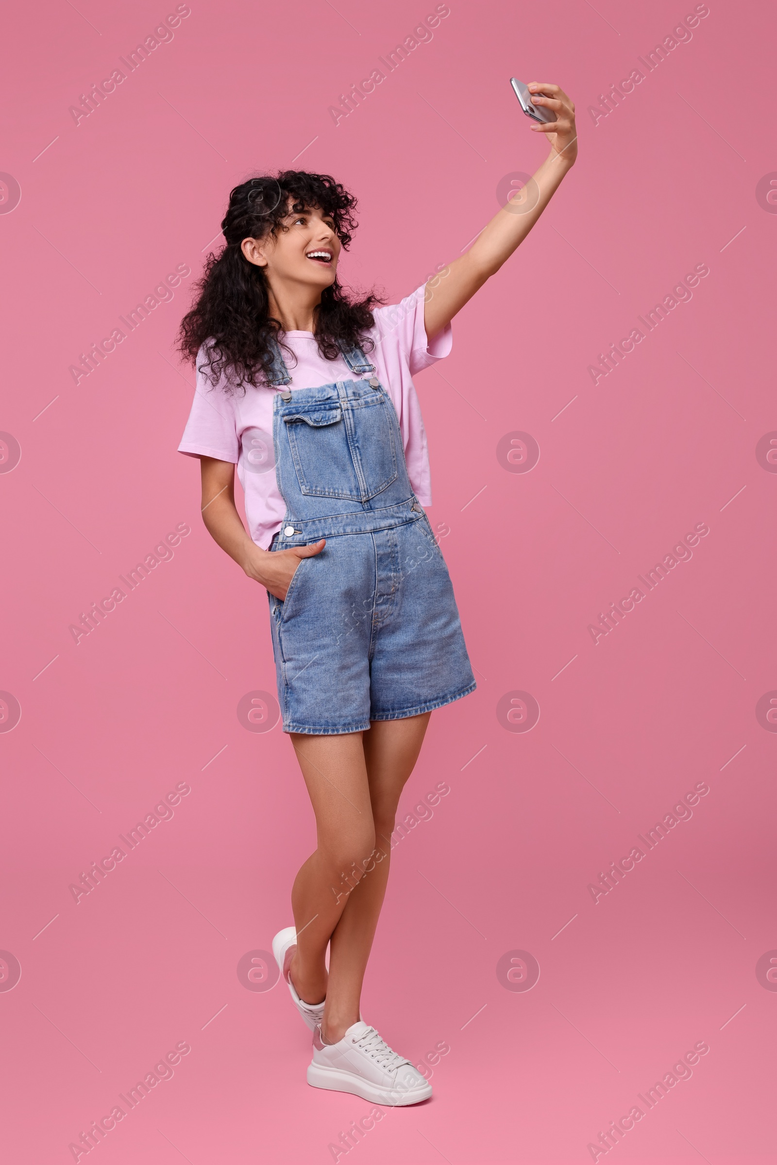 Photo of Beautiful young woman taking selfie on pink background