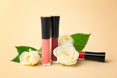 Lip glosses and flowers on color background