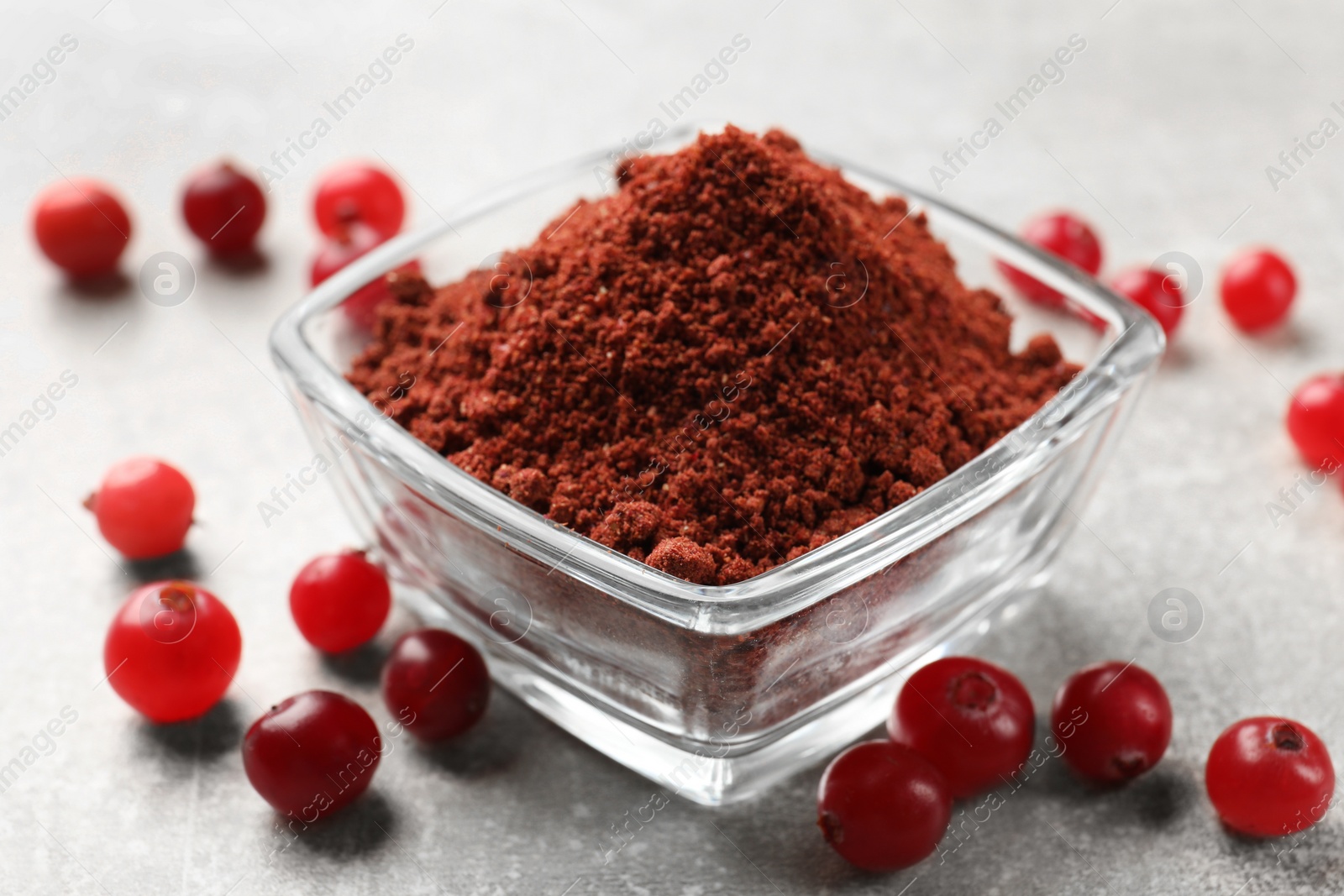 Photo of Cranberry powder in bowl and fresh berries on light grey table, closeup