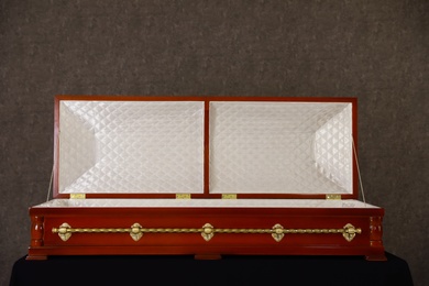 Open wooden funeral casket on stand at grey wall