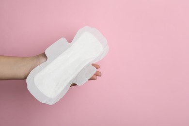 Photo of Woman holding sanitary napkin on pink background, closeup. Space for text