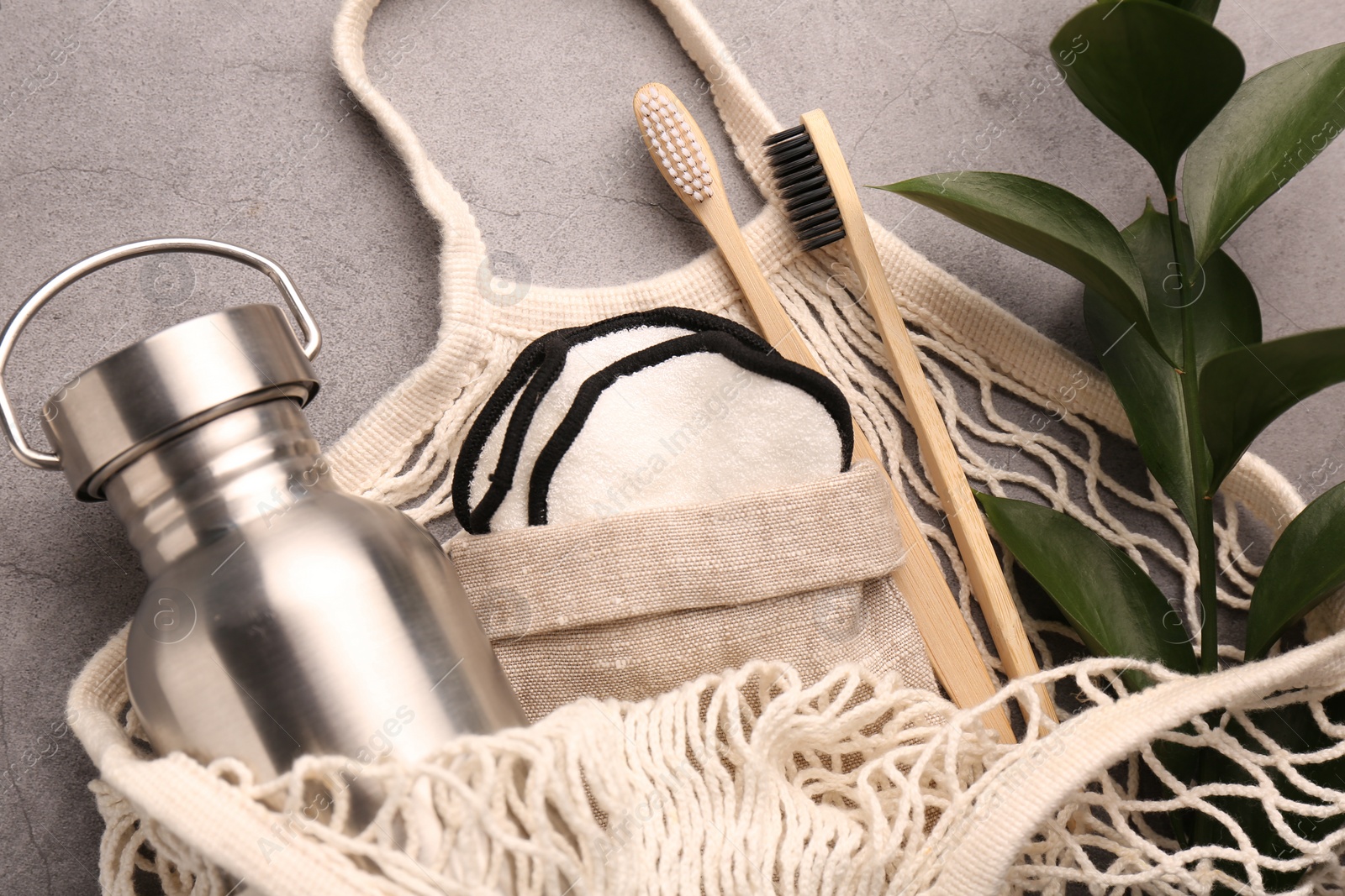 Photo of Fishnet bag with different items and green twig on grey table, top view. Conscious consumption