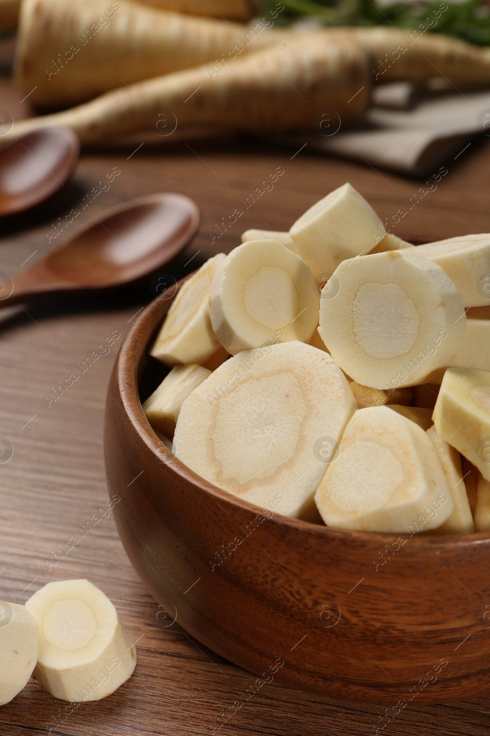 Photo of Cut fresh ripe parsnip in bowl on wooden table, closeup