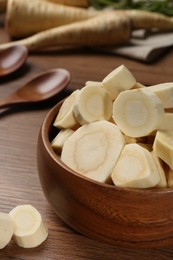 Photo of Cut fresh ripe parsnip in bowl on wooden table, closeup