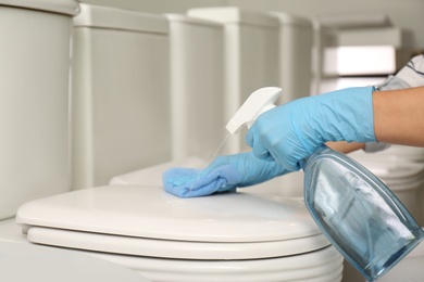 Photo of Woman cleaning toilet bowl with rag and detergent in 
store, closeup