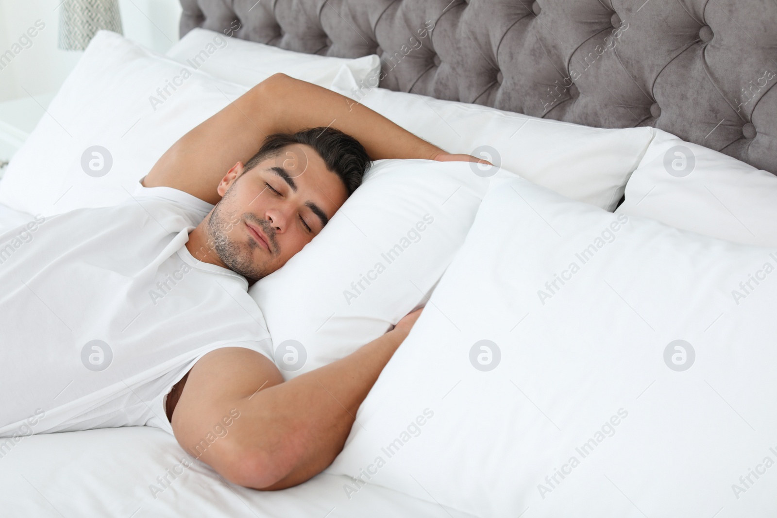Photo of Young man sleeping on bed with soft pillows at home