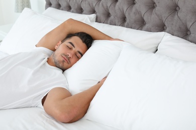 Young man sleeping on bed with soft pillows at home