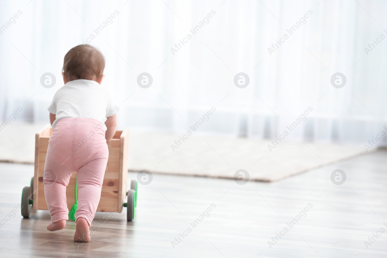 Photo of Cute baby holding on to wooden cart at home. Learning to walk