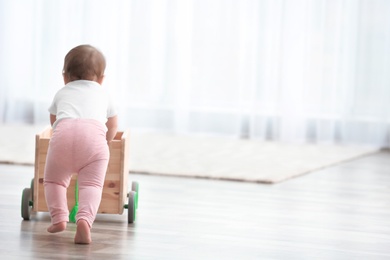 Cute baby holding on to wooden cart at home. Learning to walk