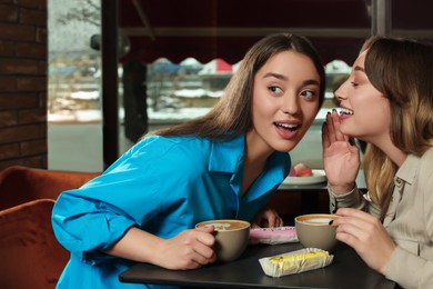 Photo of Young women with coffee and eclairs spending time together in cafe