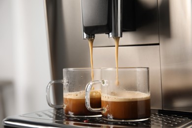 Espresso machine pouring coffee into glass cups against blurred background, closeup