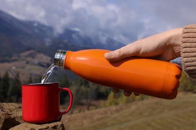 Photo of Woman pouring hot water into mug in mountains, closeup