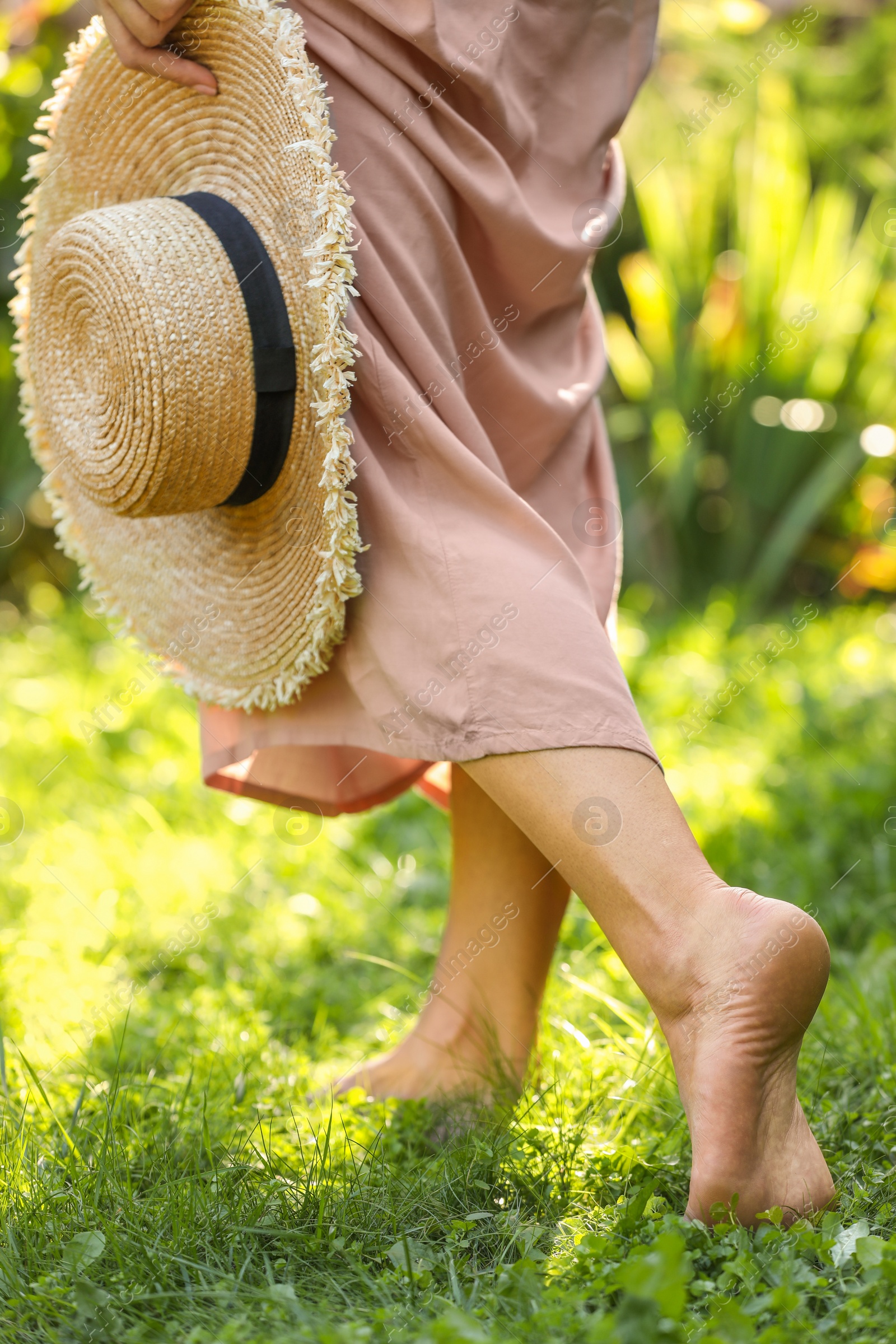 Photo of Woman with straw hat walking barefoot on green grass outdoors, closeup