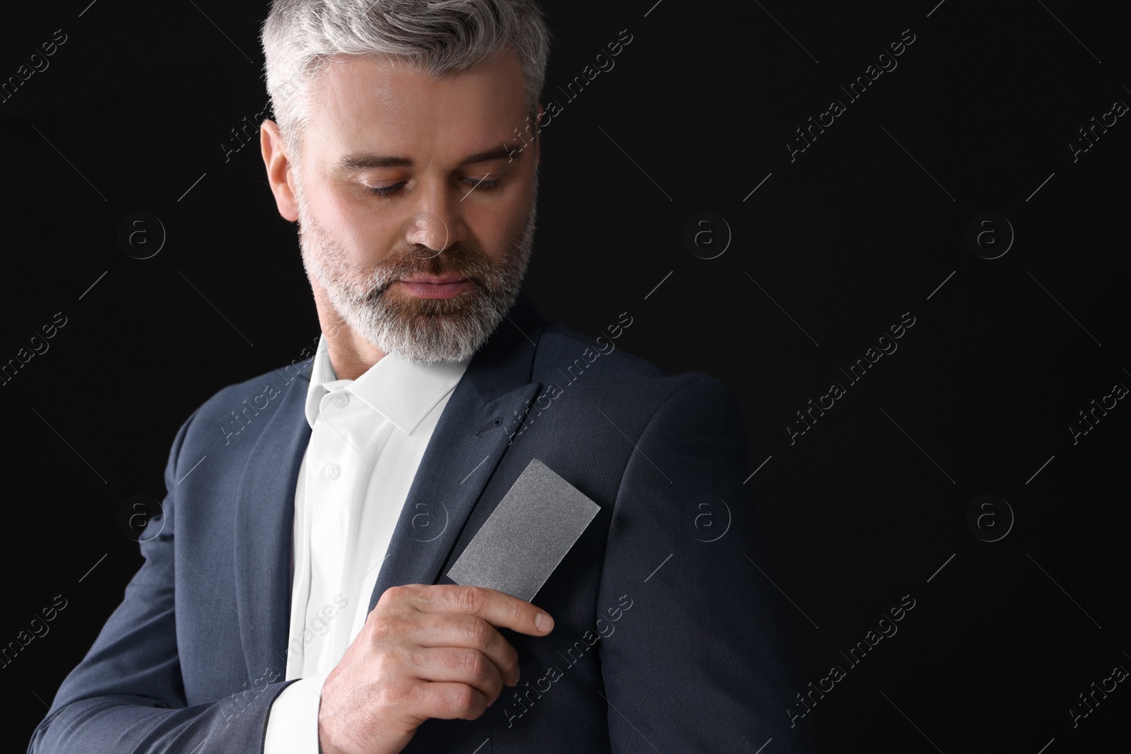 Photo of Handsome businessman holding blank business card on black background. Space for text