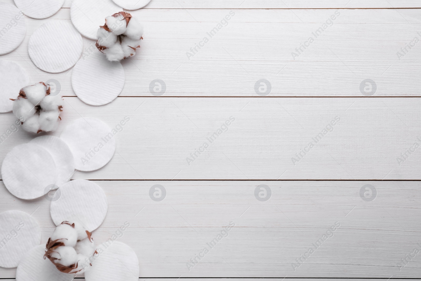 Photo of Flat lay composition with many clean cotton pads and flowers on white wooden table. Space for text