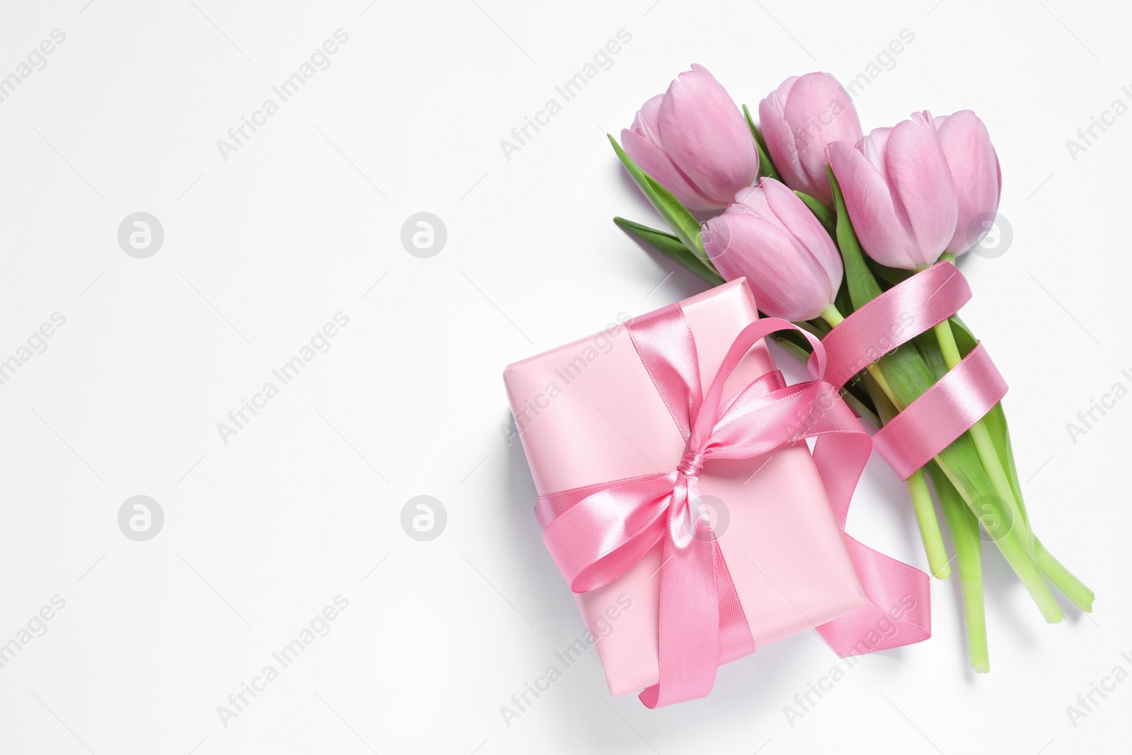 Photo of Beautiful gift box with pink bow and tulips on white background, flat lay. Space for text