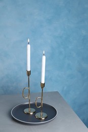 Photo of Holders with burning candles on grey table near light blue wall
