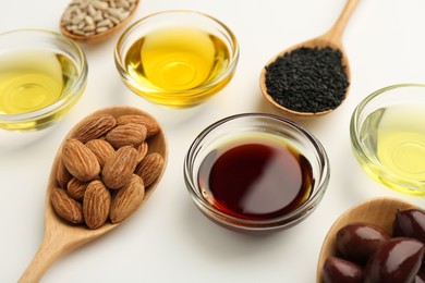 Photo of Vegetable fats. Different cooking oils in bowls and spoons with ingredients on white background, closeup