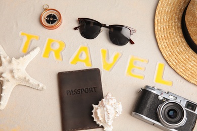 Photo of Flat lay composition with different tourist objects and word TRAVEL on sand